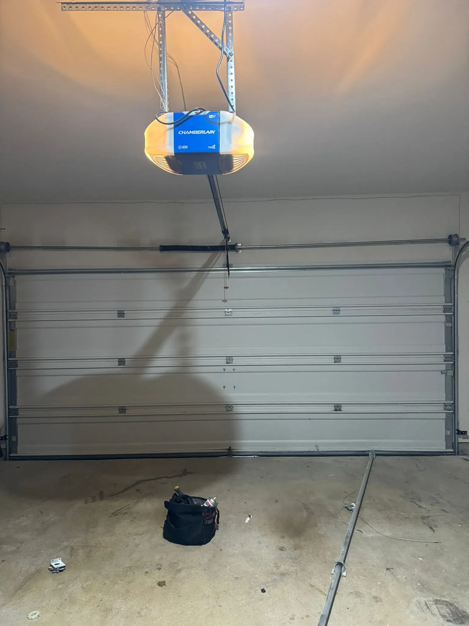 A Chamberlain opener labeled myQ, Wi-Fi and battery backup, hung from ceiling brackets above a white sectional door