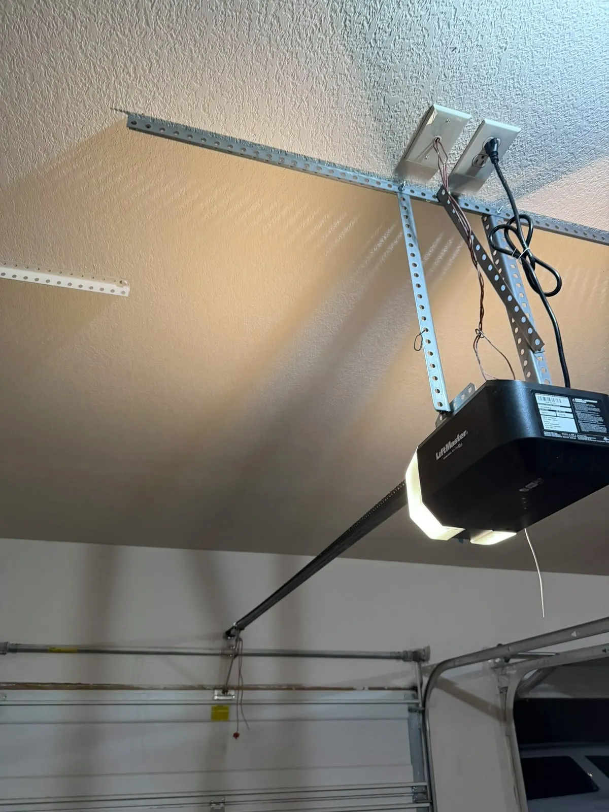 A LiftMaster garage door opener mounted on a garage ceiling, its light on